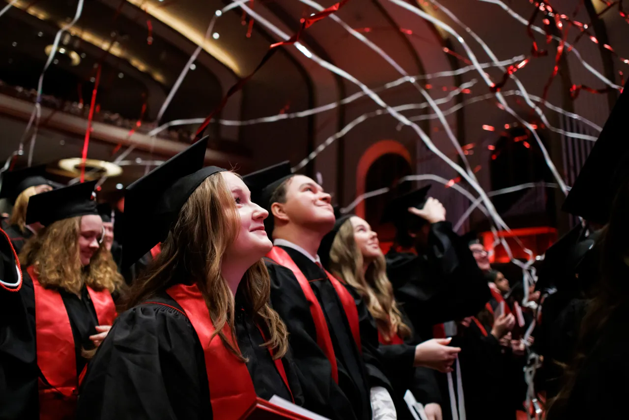 Students in graduation regalia smiling and lookup up as streamers fall on them overlayed with a red icon featuring students in caps and gowns and the text Student Success